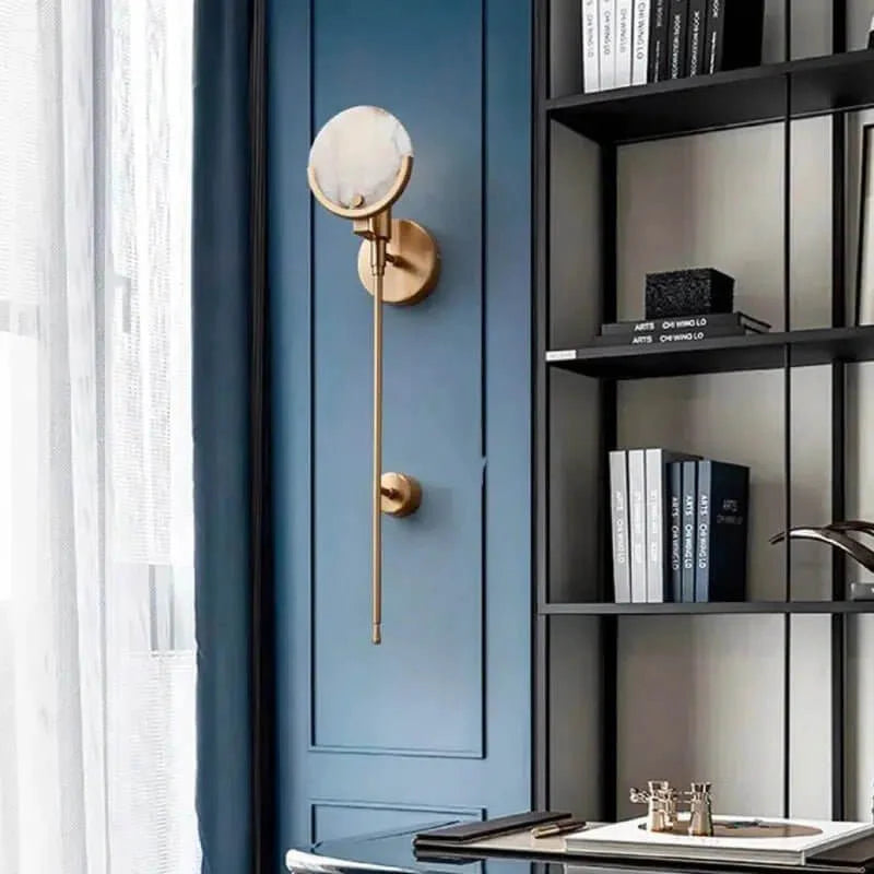 Madrid wall light with brass finish and round natural stone disc on a blue wall beside black shelving