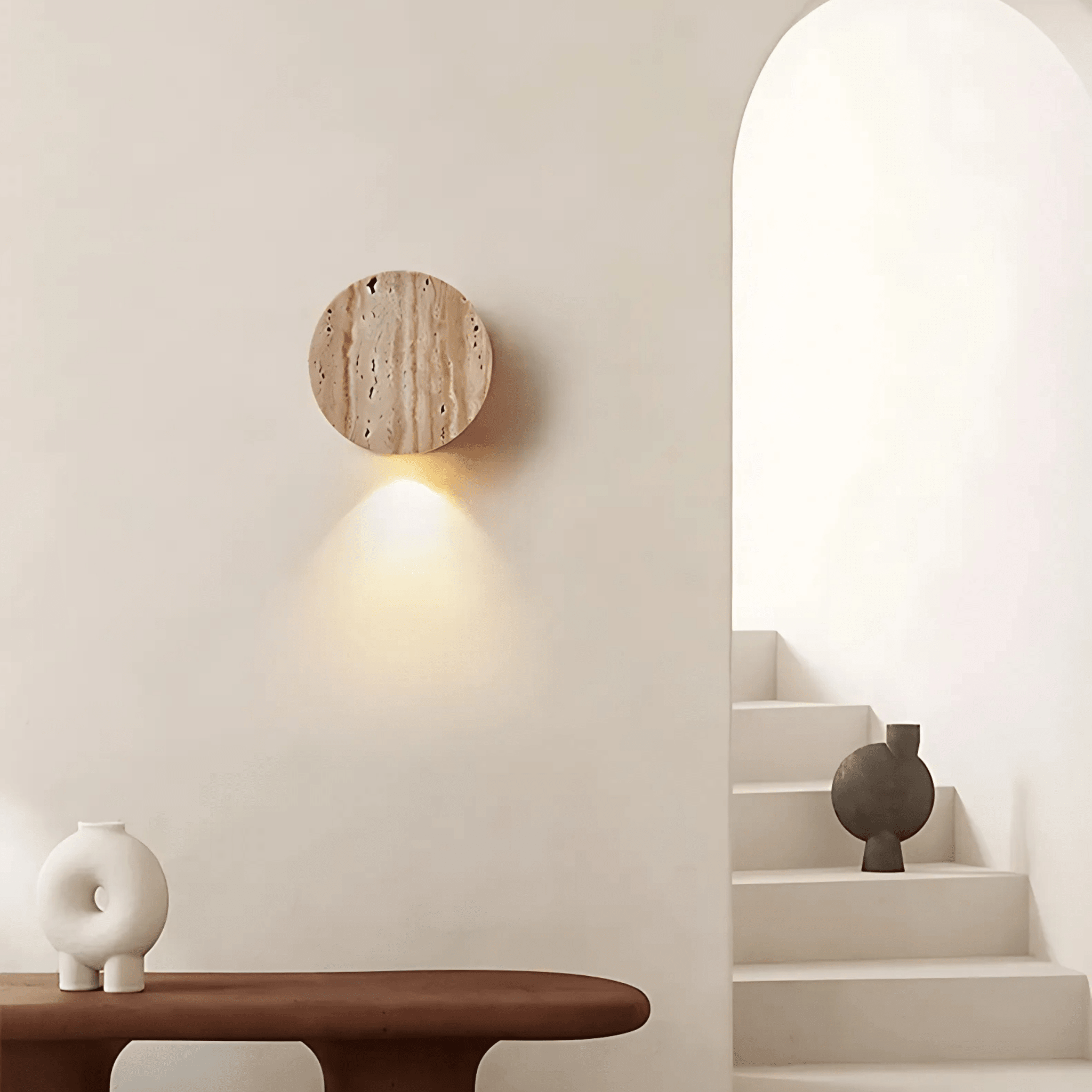 La Paz travertine wall light on a minimalist wall, casting warm light beside a modern staircase